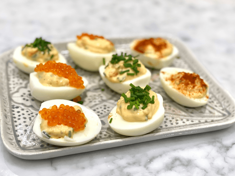 A silver tray with halved eggs topped with a salad filling and trout roe, and herbs sprinkled on top.