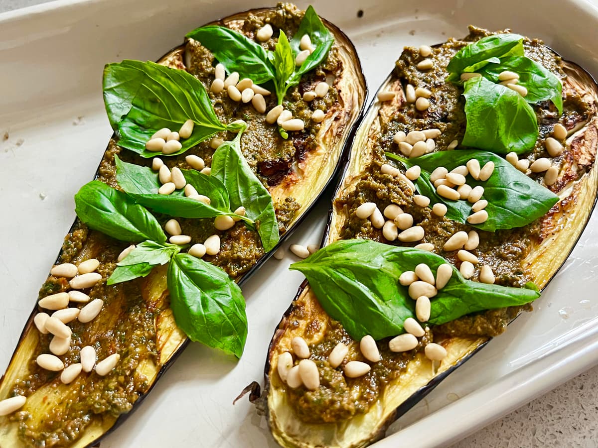 A tray of two halves of eggplant with pesto and pine nuts sprinkled on top.