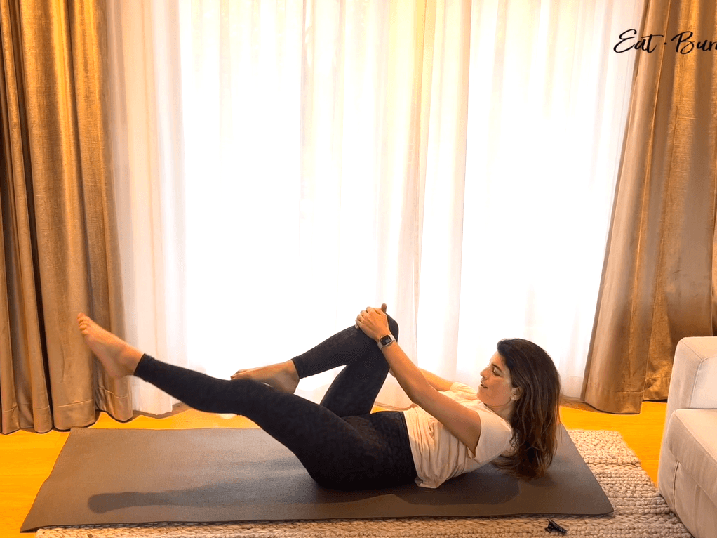 Yalda Alaoui, mid-movement on her grey mat in front of the draped window.
