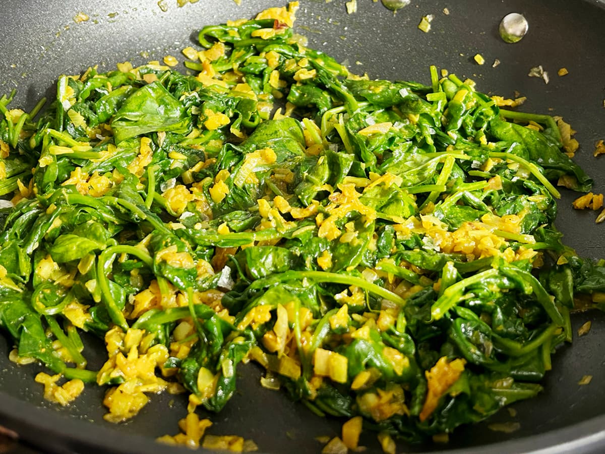 A pan of stir-fried spinach with a splash of orange from turmeric.