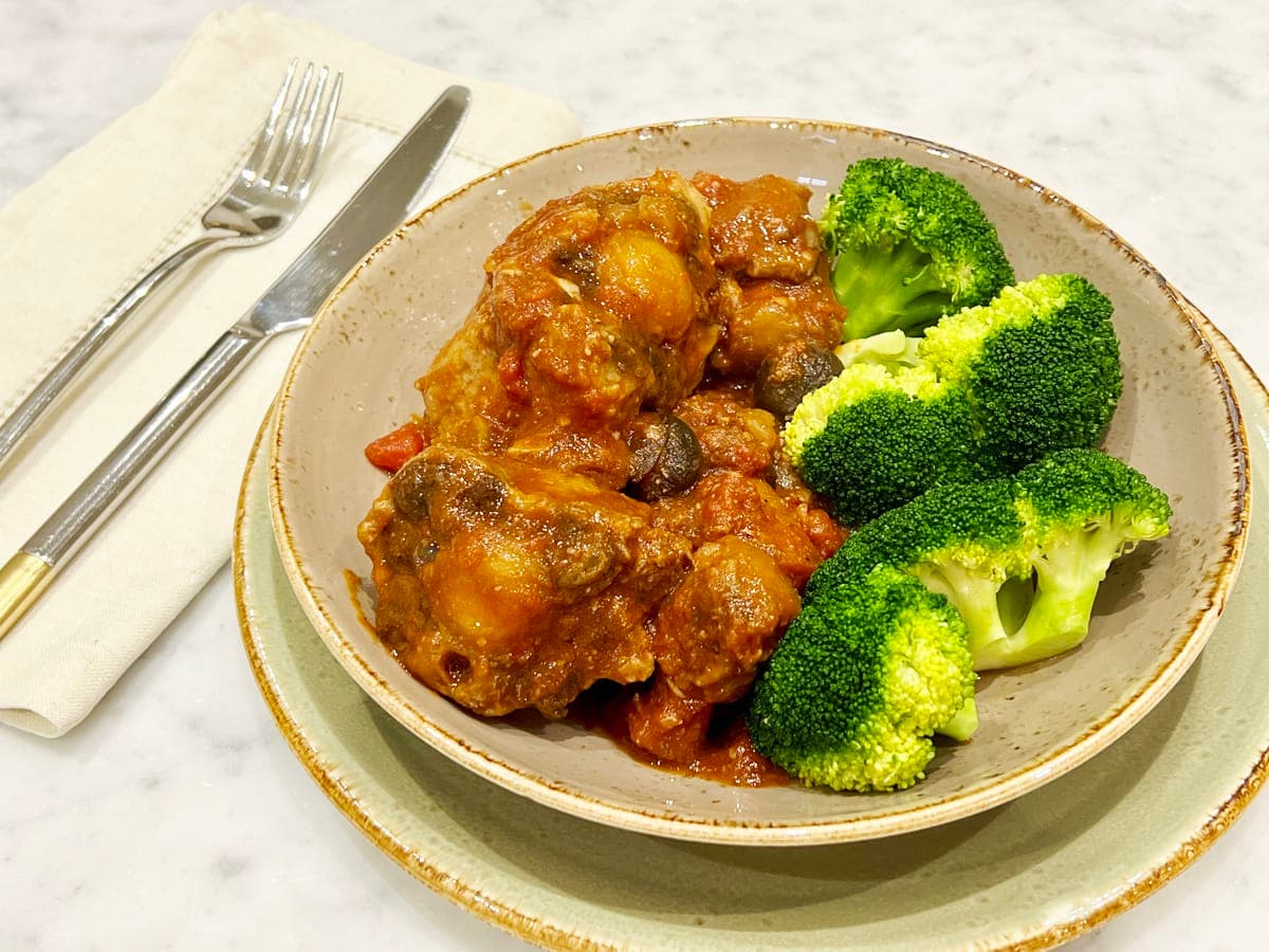 Oxtail, tomato and mushrooms stew on a plate with cooked broocoli