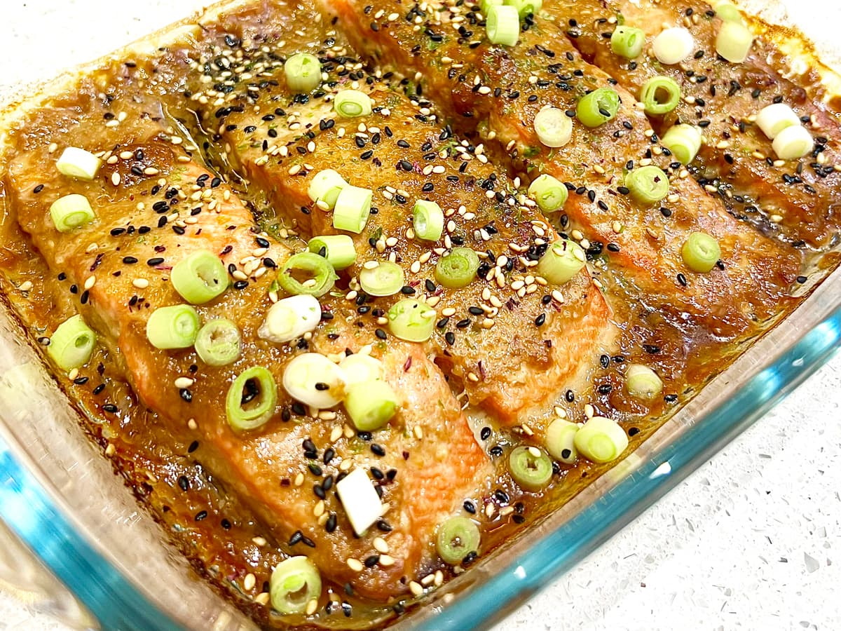 Salmon fillets in a roasting dish in a miso marinade decorated with scallions