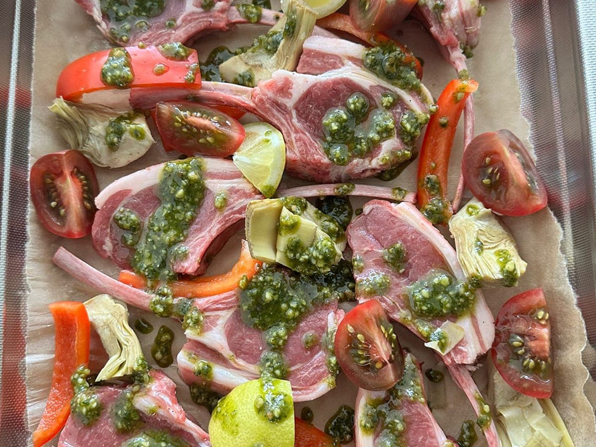 Pesto Lamb Traybake with lamb cutlets, pesto, tomates, artichokes, and peppers.